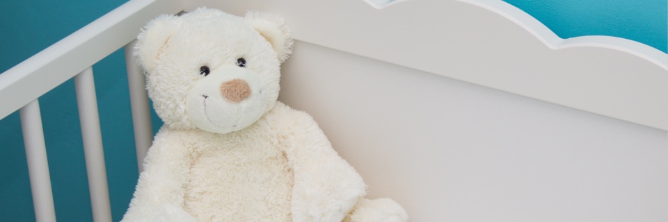 A white teddy bear is shown in a baby's cot