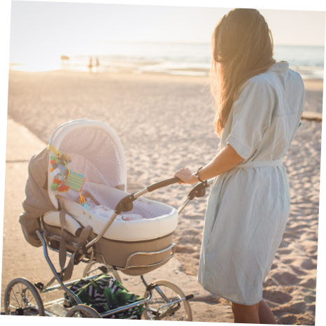 A mother watches over her newborn in a pram whilst taking a stroll on the beach