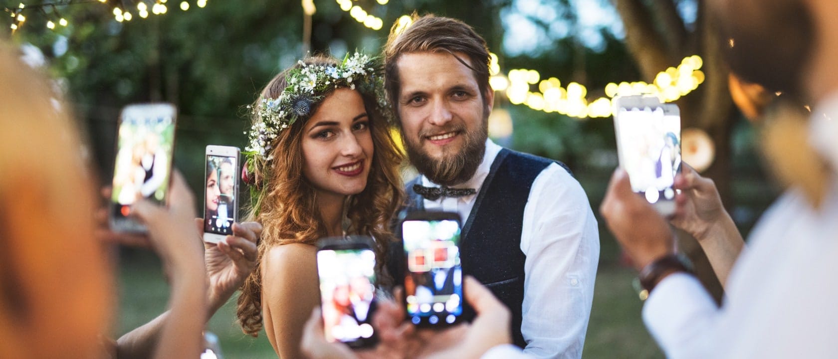 Man and woman on wedding day posing for photos while lots of people take pictures on their phones