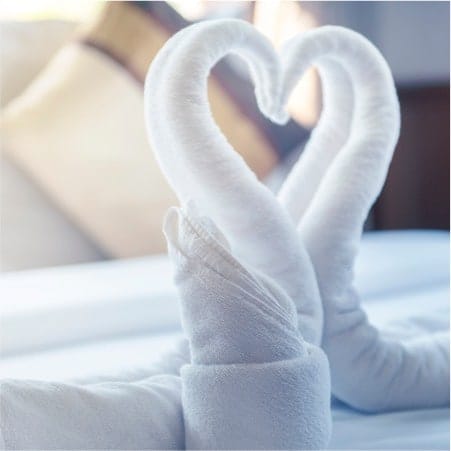 Towels on a bed that have been folded to look like swans heads forming a heart