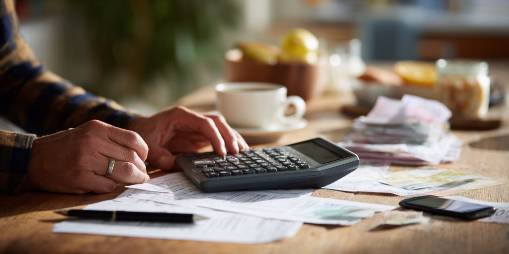 Person calculating small loan repayments on calculator with bills on kitchen table